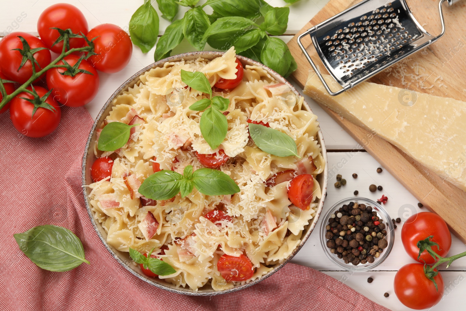 Photo of Plate of delicious pasta with tomatoes, basil and parmesan cheese near ingredients on white wooden table, flat lay