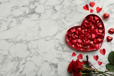 Photo of Heart shaped chocolate candies and bouquet on white marble table, flat lay. Space for text
