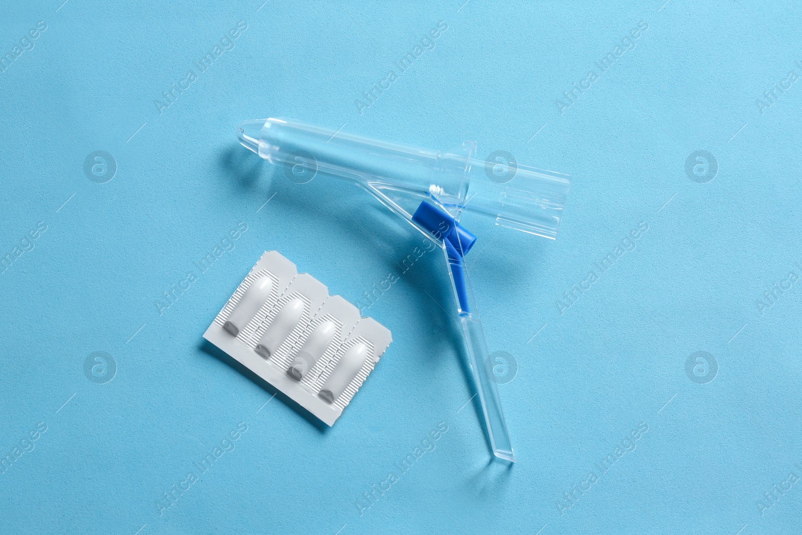 Photo of Anoscope and suppositories on light blue background, flat lay. Hemorrhoid treatment