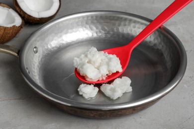 Photo of Frying pan with coconut oil and spoon on light grey table