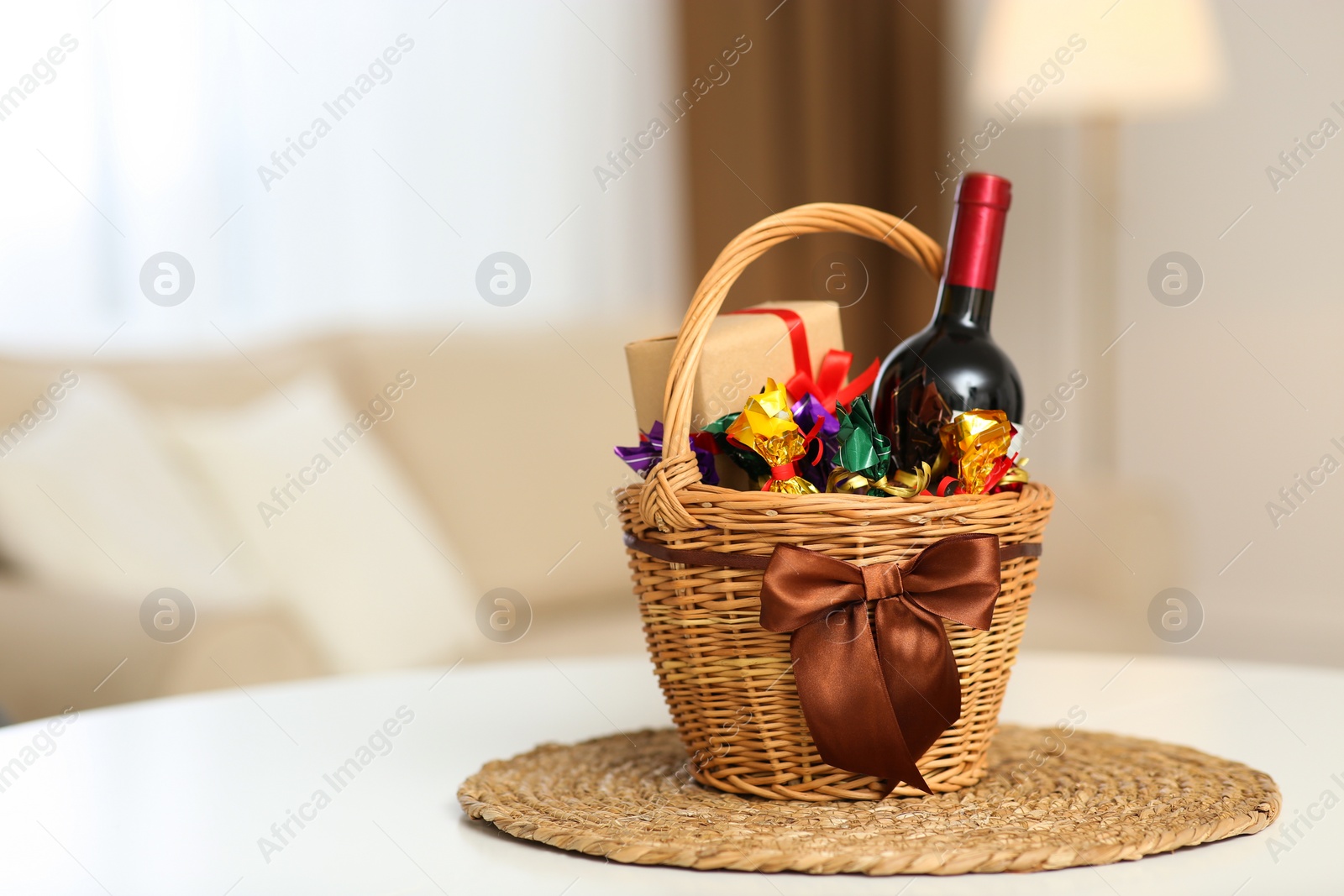 Photo of Wicker basket full of gifts on white table in living room. Space for text