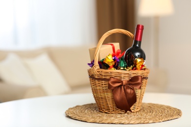 Wicker basket full of gifts on white table in living room. Space for text