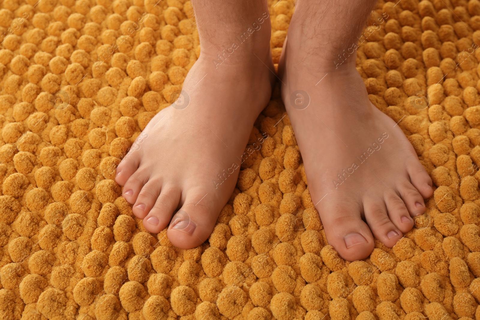 Photo of Man standing on soft orange bath mat, closeup