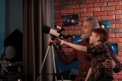 Photo of Little boy with his grandfather using telescope to look at stars in room