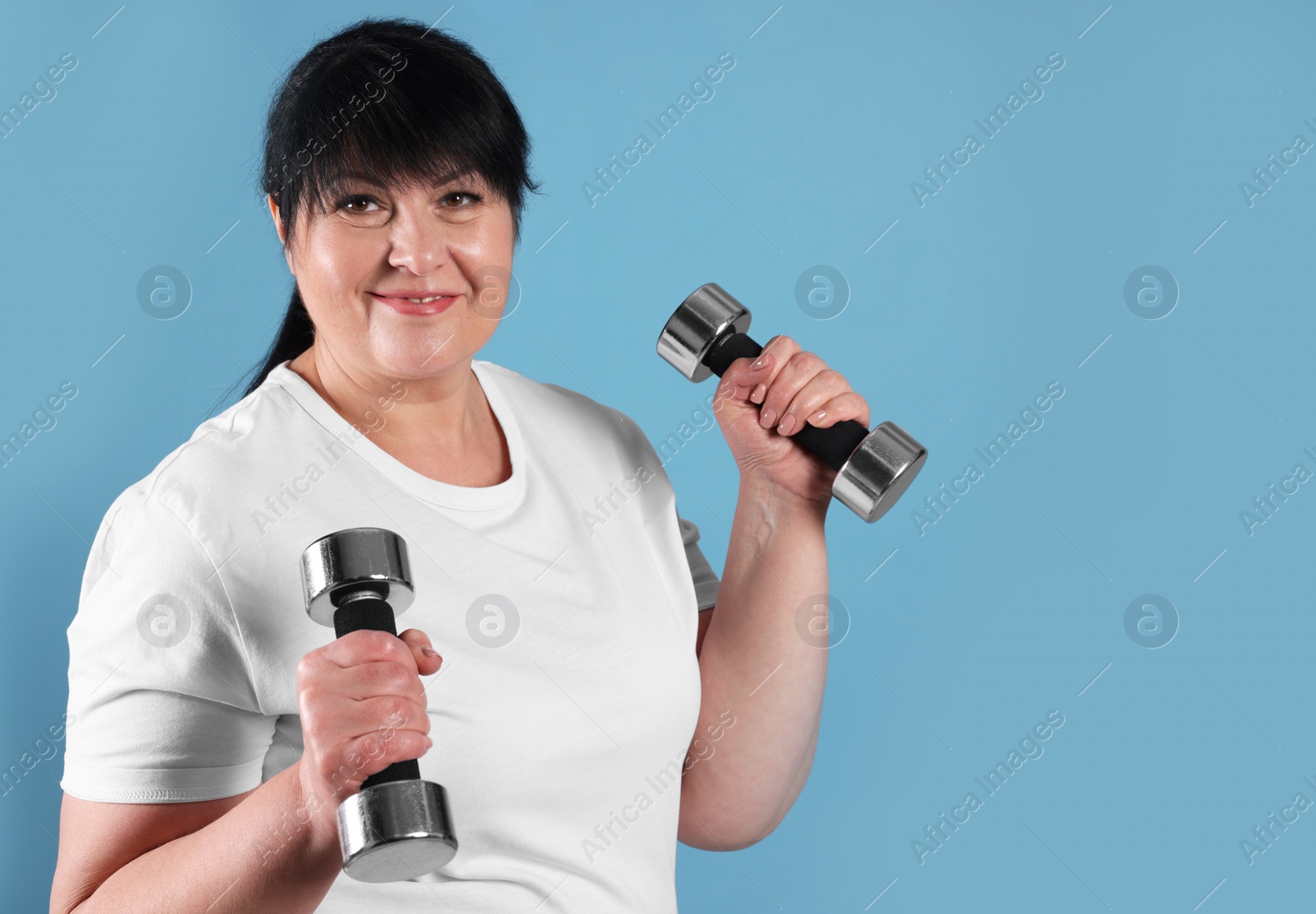 Photo of Happy overweight mature woman doing exercise with dumbbells on light blue background