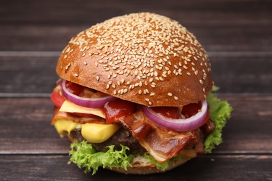 Photo of Delicious burger with bacon, patty and vegetables on wooden table, closeup