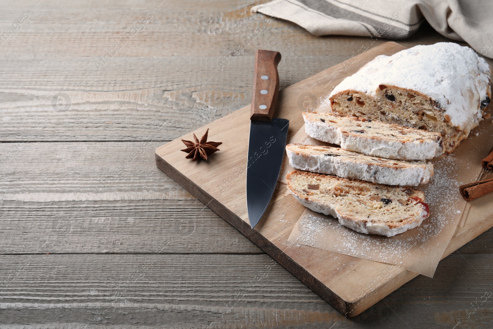 Photo of Traditional Christmas Stollen with icing sugar on wooden table, space for text