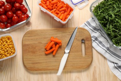 Photo of Board with baby carrots, knife and containers with fresh products on wooden table, flat lay. Food storage