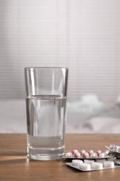 Glass of water and different pills in blisters on wooden table indoors
