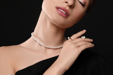 Photo of Young woman wearing elegant pearl jewelry on black background, closeup