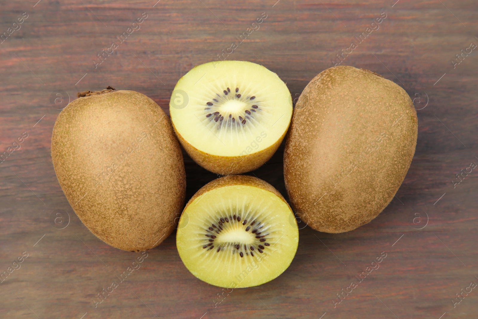 Photo of Whole and cut ripe yellow kiwis on wooden table, flat lay