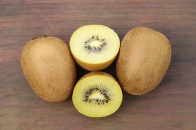 Photo of Whole and cut ripe yellow kiwis on wooden table, flat lay