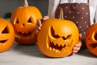 Photo of Woman with carved pumpkins for Halloween at white marble table, closeup