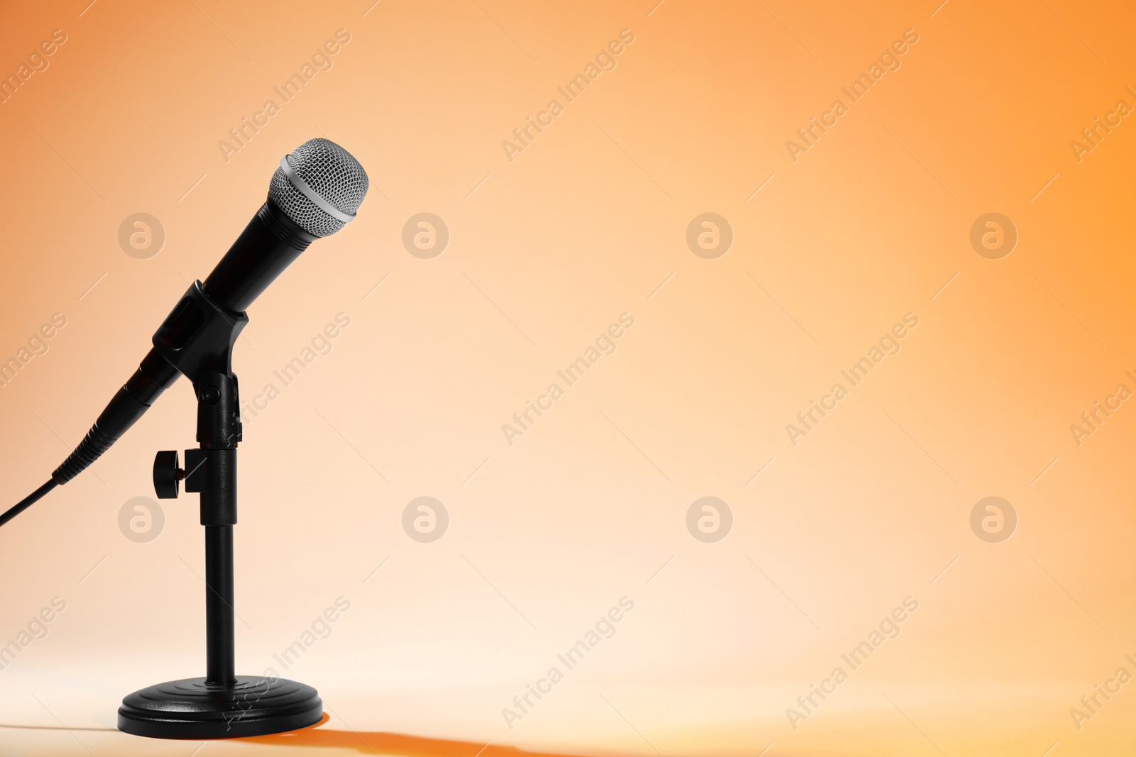 Photo of Modern microphone on stand against color background. Space for text