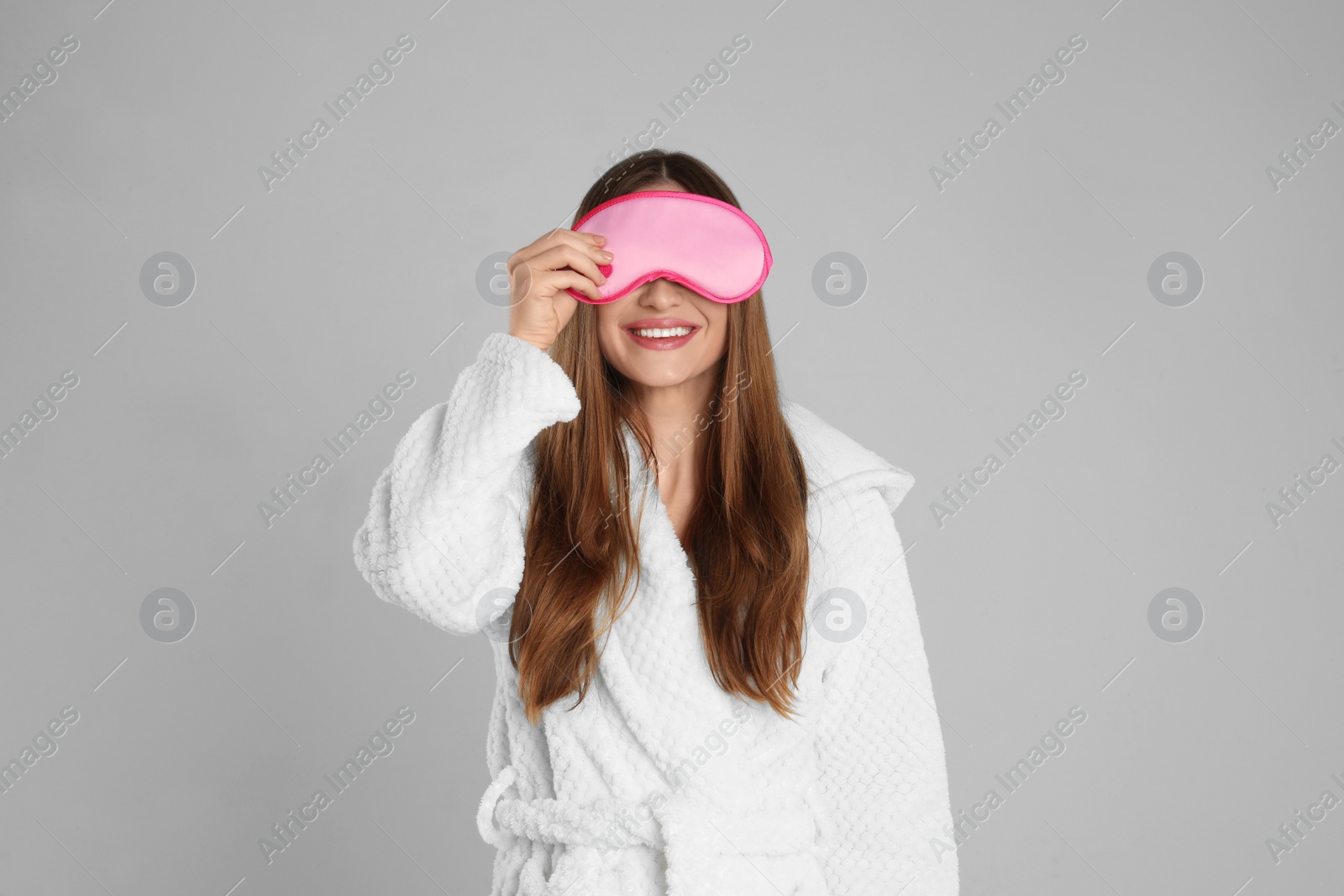 Photo of Young woman in bathrobe and eye sleeping mask on light grey background