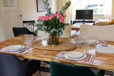 Beautiful table setting with bouquet of roses, napkins and candles in room