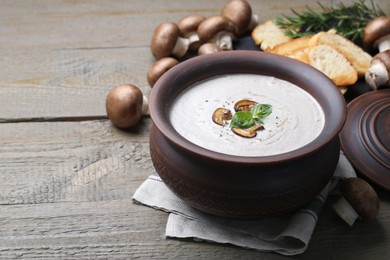 Photo of Delicious homemade mushroom soup in ceramic pot and fresh ingredients on wooden table. Space for text