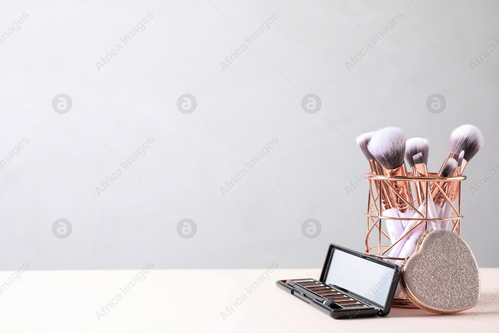 Photo of Make up brushes in holder and cosmetic products on white table. Space for text