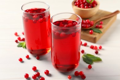 Tasty cranberry juice in glasses and fresh berries on white wooden table, closeup