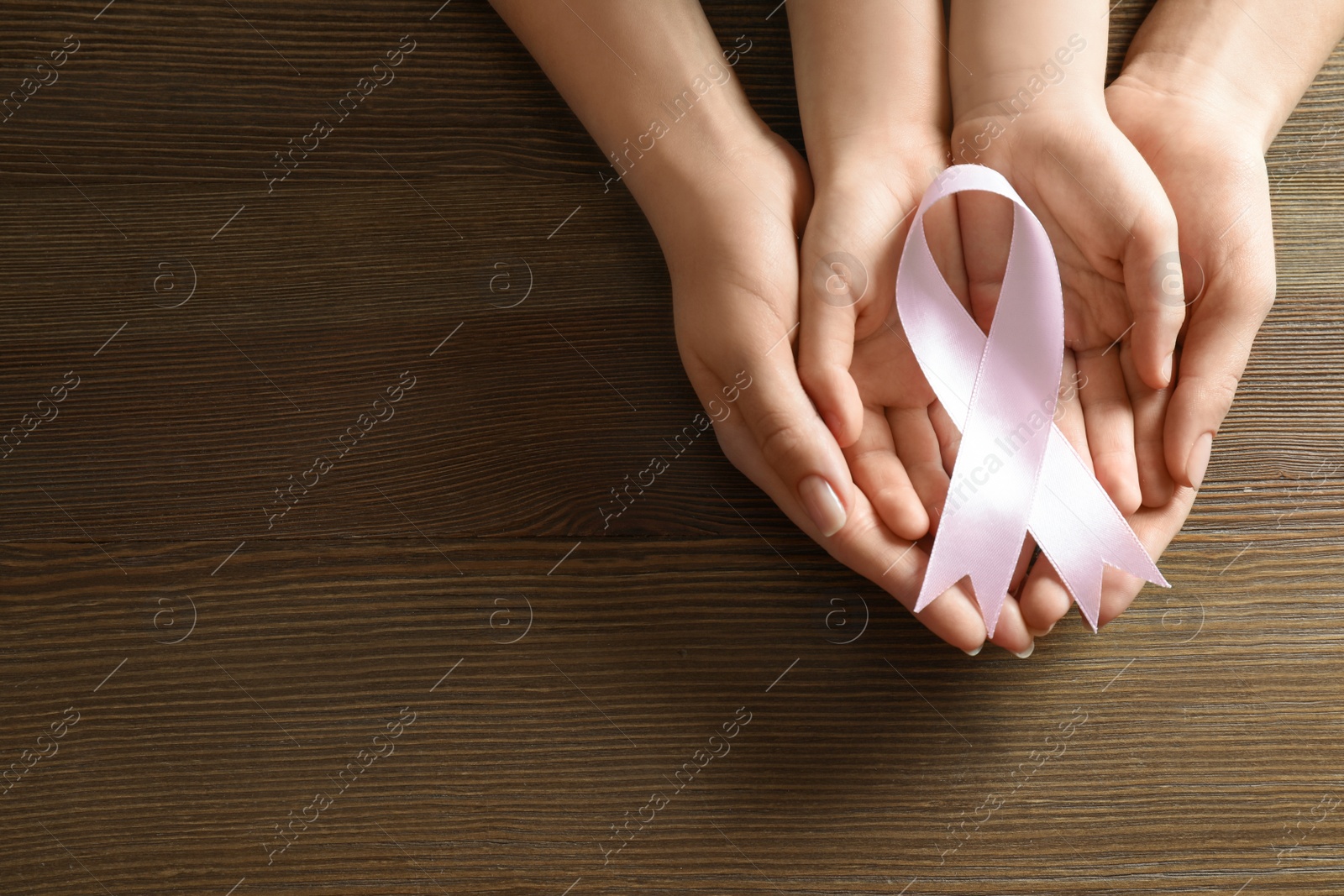 Photo of Woman and child holding pink ribbon on wooden background, top view with space for text. Breast cancer awareness