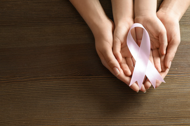 Woman and child holding pink ribbon on wooden background, top view with space for text. Breast cancer awareness