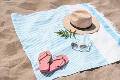 Beach towel with straw hat, sunglasses, leaves and flip flops on sand