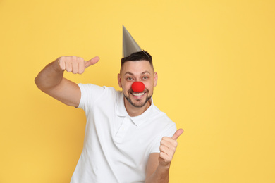 Funny man with clown nose and party hat on yellow background. April fool's day