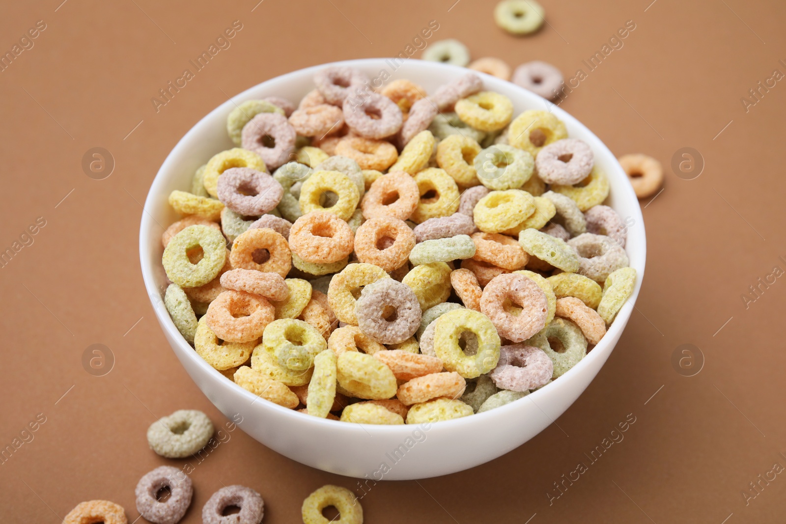 Photo of Tasty cereal rings in bowl on brown table, closeup