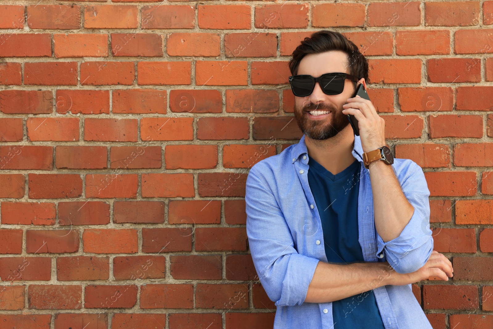 Photo of Happy man talking on phone near red brick wall. Space for text