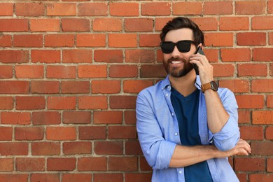 Happy man talking on phone near red brick wall. Space for text