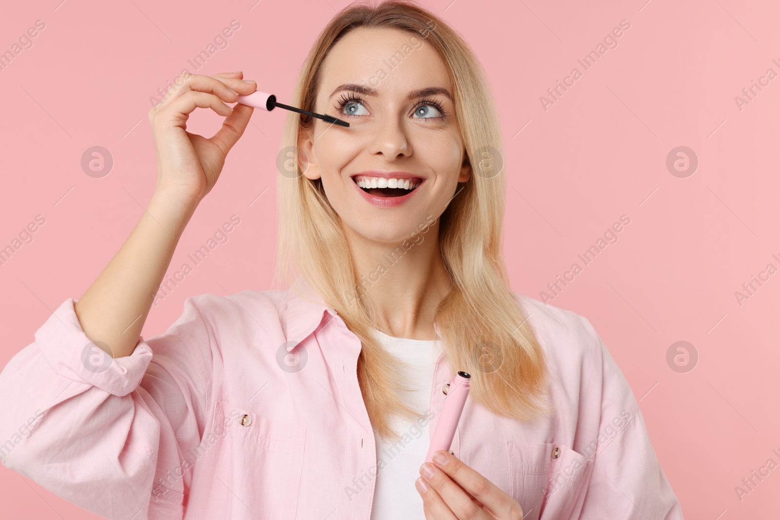 Photo of Beautiful woman applying mascara on pink background