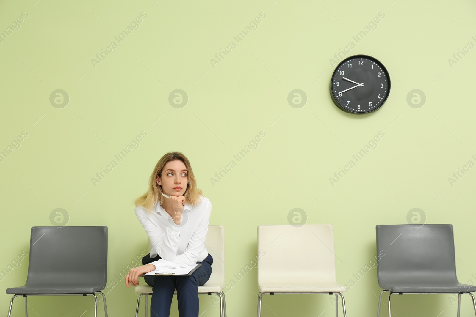 Photo of Young woman with clipboard waiting for job interview indoors