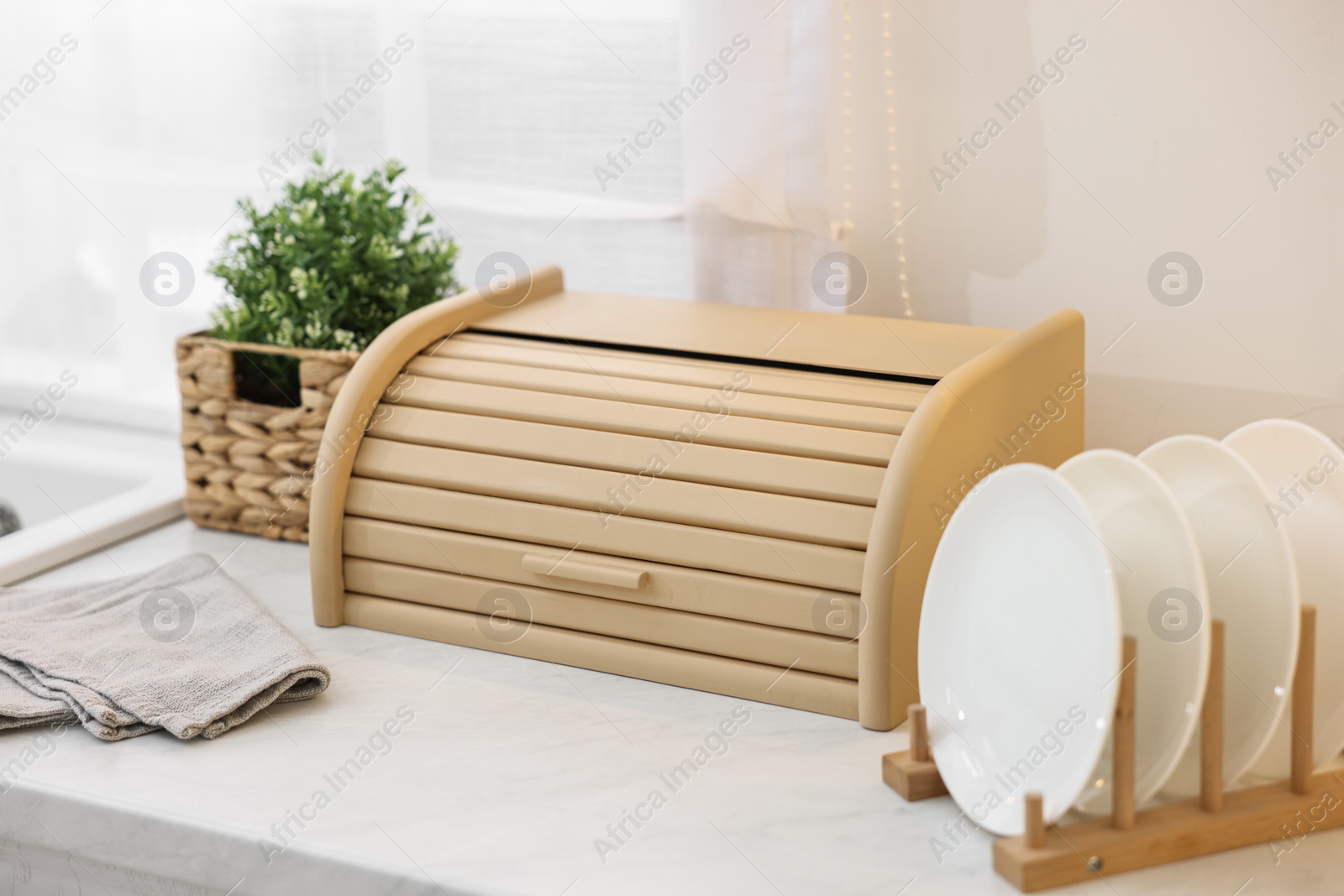 Photo of Wooden bread box, houseplant and plates on white marble countertop in kitchen