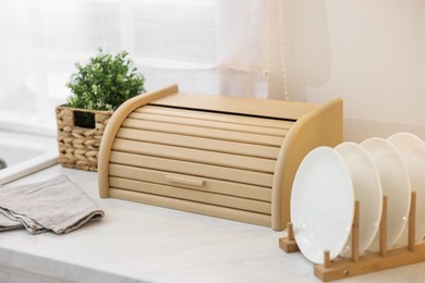 Wooden bread box, houseplant and plates on white marble countertop in kitchen