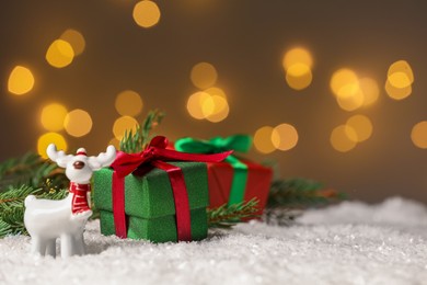 Photo of Gift boxes and Christmas decor on artificial snow against blurred festive lights, space for text