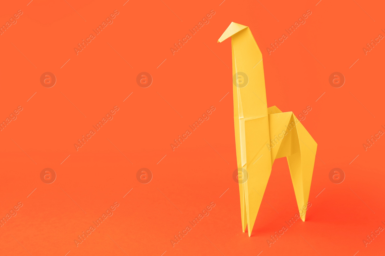 Photo of Origami art. Handmade yellow paper giraffe on orange background, space for text