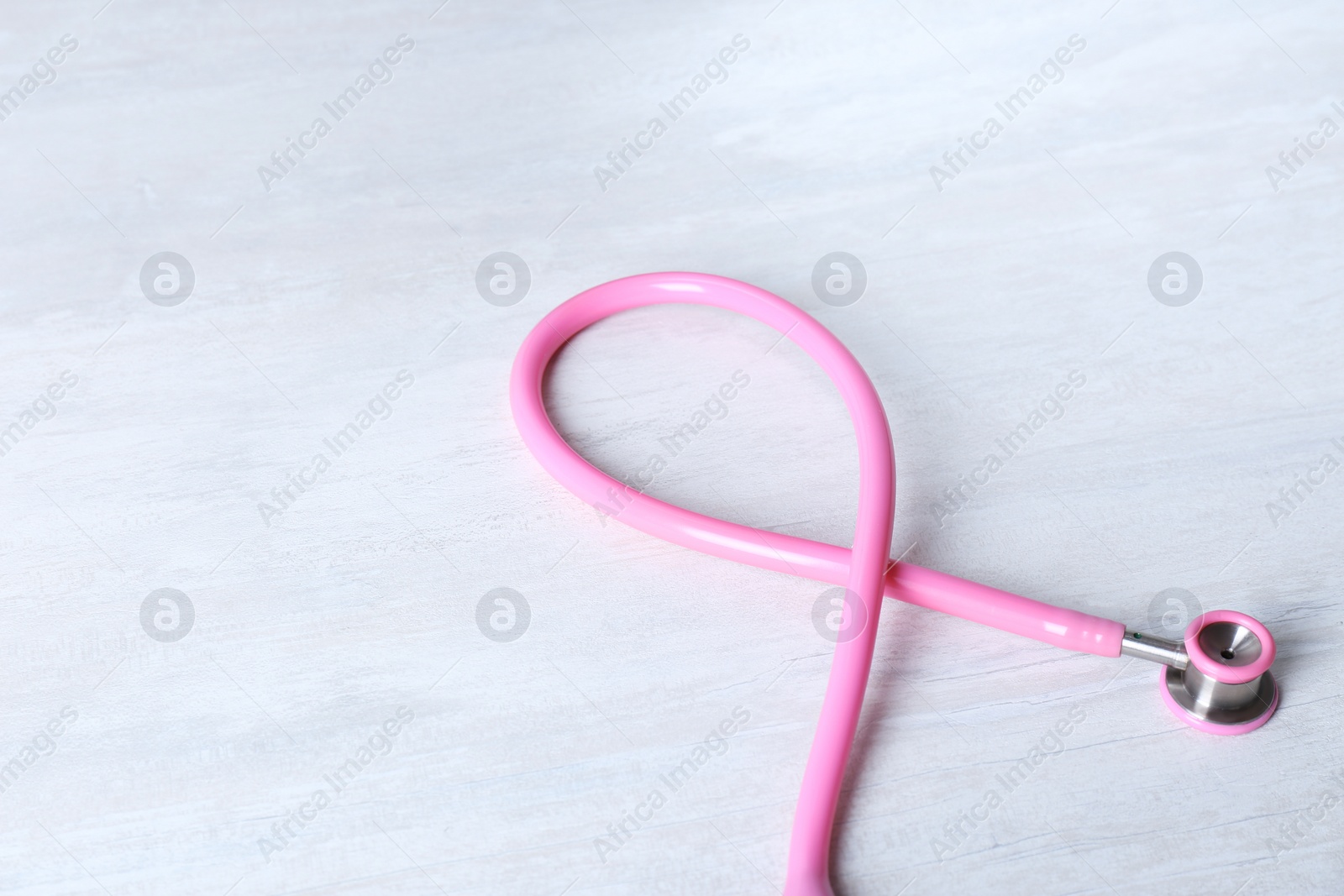 Photo of Pink stethoscope as awareness ribbon on light background. Breast cancer concept