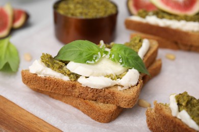 Photo of Tasty bruschetta with cream cheese, pesto sauce and fresh basil on parchment paper, closeup