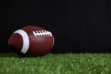 Photo of American football ball on green grass against black background. Space for text