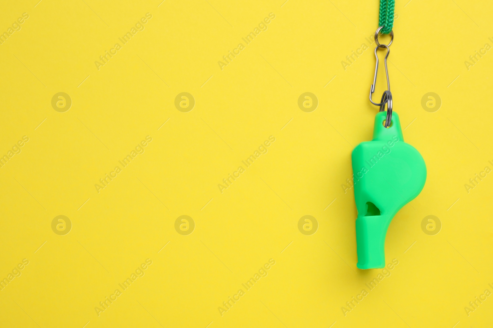 Photo of One green whistle with cord on yellow background, top view. Space for text