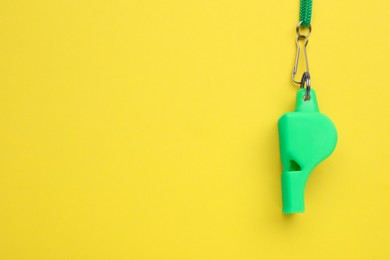 One green whistle with cord on yellow background, top view. Space for text