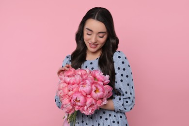 Beautiful young woman with bouquet of peonies on pink background