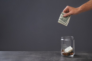Photo of Man putting money into donation jar on table against grey background, closeup. Space for text