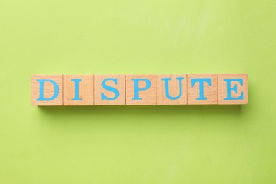 Word Dispute made with wooden cubes on light green background, top view