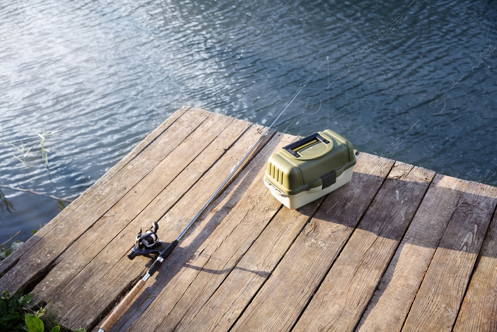 Photo of Tackle box and rod for fishing on wooden pier at riverside. Recreational activity