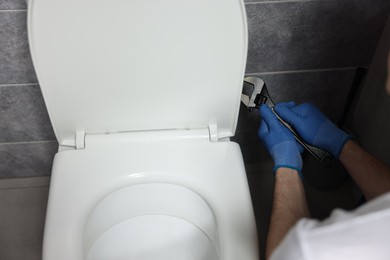 Photo of Plumber with spanner repairing toilet bowl in water closet, closeup