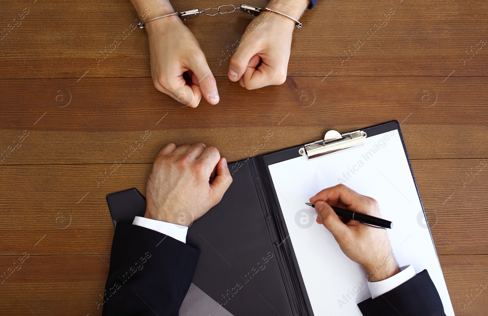 Photo of Police officer interrogating criminal in handcuffs at desk, top view