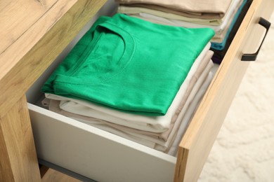Photo of Stacks of different folded shirts in drawer indoors, closeup. Organizing clothes