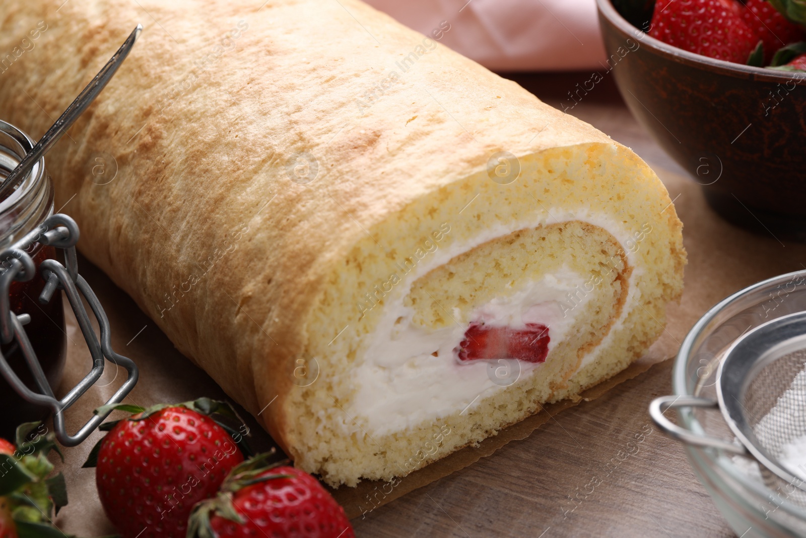 Photo of Delicious sponge cake roll with strawberries and cream on wooden table, closeup