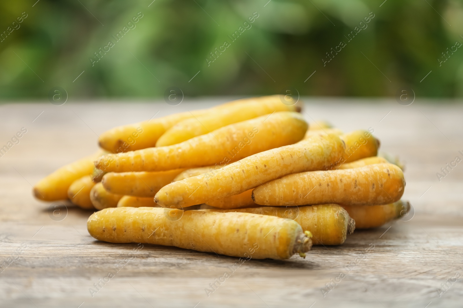 Photo of Raw yellow carrots on wooden table against blurred background